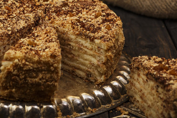 Napoleon's cake with custard is decorated with raisins and grated chocolate on a silver platter on a wooden table. Dessert Napoleon cake chopped. Napoleon cake tasty close-up.
