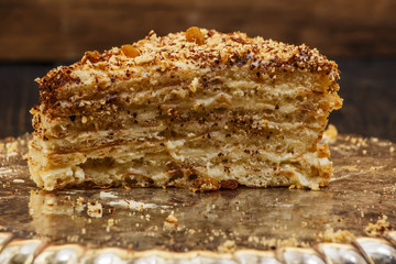 Napoleon's cake with custard is decorated with raisins and grated chocolate on a silver platter on a wooden table. Dessert Napoleon cake chopped. Napoleon cake tasty close-up.

