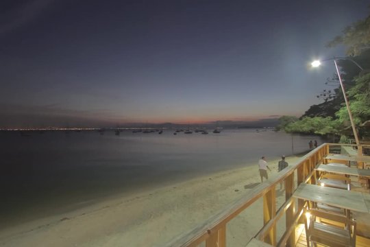 Time lapse - Sunset with colorful sky at 'Santo Ant&ocirc;nio de Lisboa' beach, wooden deck and chairs in the foreground. Boats moored in the sea. Florian&oacute;polis, Santa Catarina / Brazil