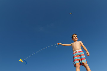 Fototapeta na wymiar boy with a kite against the blue sky. child launches kite on the beach. Copy space for your text