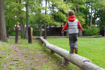 little child on the balance beam. boy walking on a log in the park. Back view. Copy space for your text