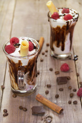 Delicious milkshake with ice cream, raspberries, chocolate, cinnamon and coffee beans on wooden background