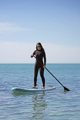 Young Woman Stand Up Paddle Boarding in Blue Sea