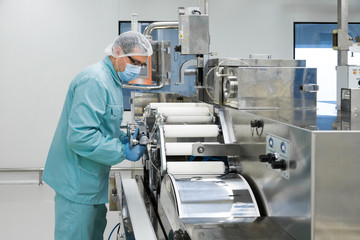 Pharmacy industry factory man worker in protective clothing in sterile working conditions operating on pharmaceutical equipment
