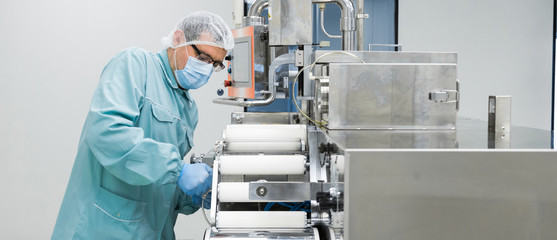 Naklejka premium Pharmacy industry factory man worker in protective clothing in sterile working conditions operating on pharmaceutical equipment