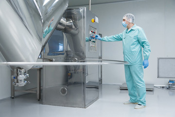 Pharmaceutical factory man worker in protective clothing working with control panel in sterile working conditions