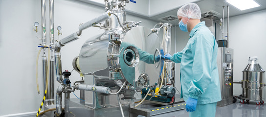 Pharmaceutical factory man worker in protective clothing working on equipment in sterile working conditions