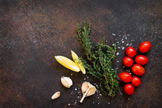 Ingredients for cooking on a dark stone table - thyme, cherry tomato, garlic and lemon. Copy space, top view flat lay background.
