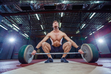 Muscular fitness man preparing to deadlift a barbell over his head in modern fitness center.Functional training.Snatch exercise.