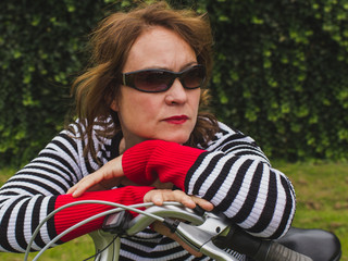 Portrait of attractive  senior brunette with sunglasses and  leaning on bicycle. Leisure concept.