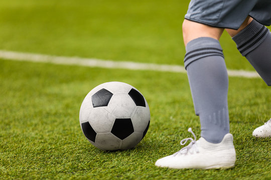 Football detail. Kicking the soccer ball. Football player feet and classic soccer ball on grass pitch.