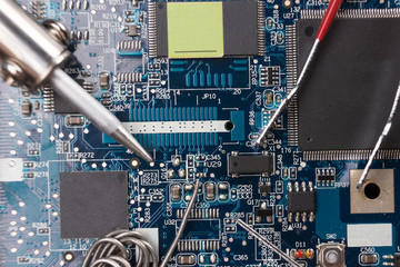 Tin the soldering iron and tweezers on the background of the motherboard. Macrophotography.