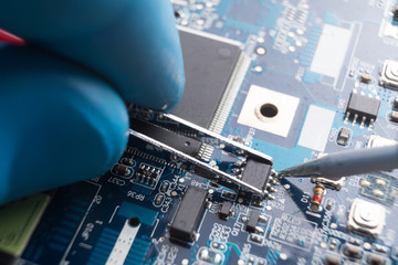 Hand with tweezers holding the chip, soldering iron solder it in place. Computer repair. Macrophotography. Copy space.