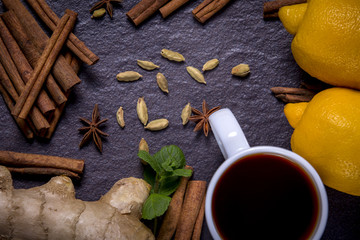 Tea, lemon, ginger, mint, cinnamon stick, cardamom, spices on black stone background