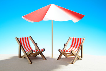 Two chaise longue under an umbrella on the sandy beach, sky with copy space