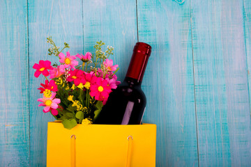 bottle of wine and flowers in the package on wooden background, space for text