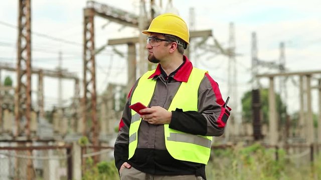 Workman at electric power plant uses smartphone. Power engineering specialist with cell phone in hand on electric power station