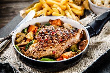 Grilled steak with french fries and vegetables served on black stone on wooden table