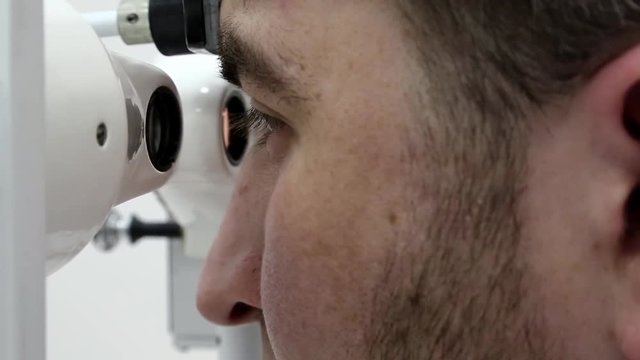 Man in ophthalmology clinic. Patient looks in synoptophore - ophthalmic instrument, used for diagnosing imbalance of eye muscles and treating them by orthoptic methods, for treatment of strabismus