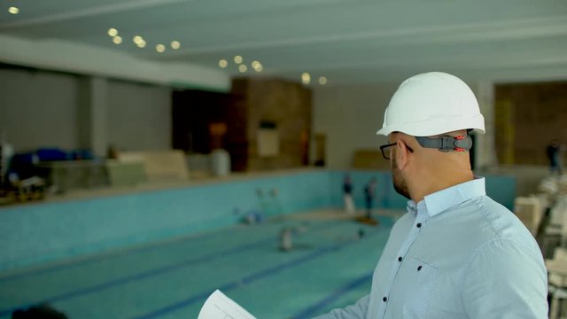 engineer looking at building plans in construction site. on the background of the pool under construction. 4 k the design of the pool. construction of the pool. Spa salon construction. Empty swimming