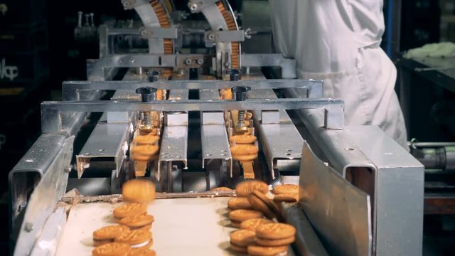 Industrial machine is producing biscuits and is being controlled by a female worker
