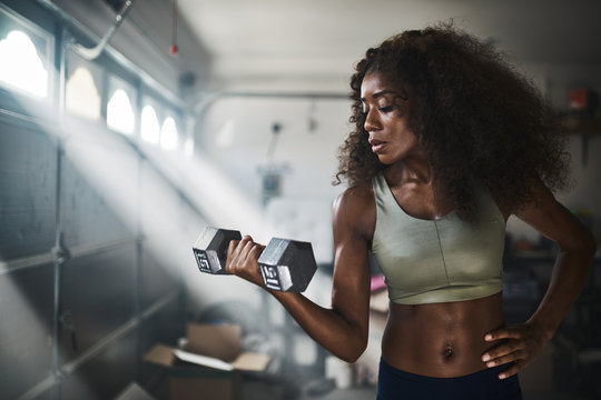 fit african american woman working out by lifting weights in home gym