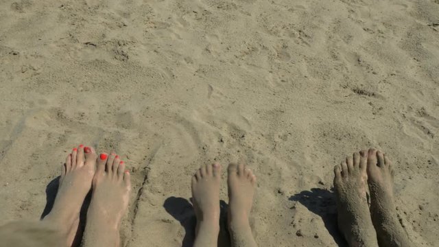 Bare feet of a family on the shore. Legs in the sand. The feet are sprinkled with sand. People make moves with their feet.