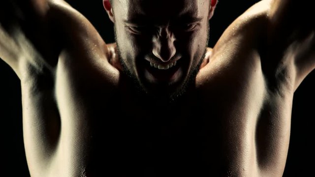 Hard training of sportsman with barbell. Close up young handsome man doing strength training on dark background.