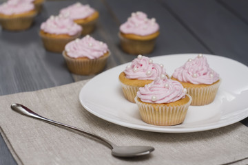 four cupcakes on grey wooden table, three cupcakes on oval white plate.