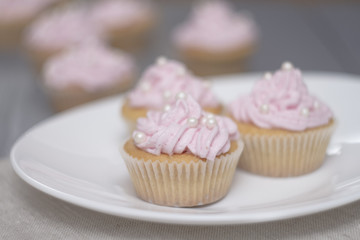 four cupcakes on grey wooden table, three cupcakes on oval white plate. Close up