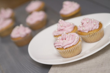 four cupcakes on grey wooden table, three cupcakes on oval white plate. Holland angle