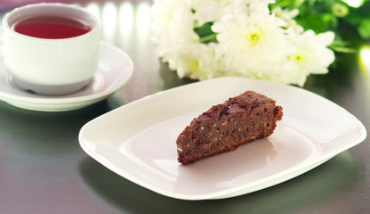 brownie cake on a white plate decorated with chrysanthemum flowers prepared for tea with a mug of tea