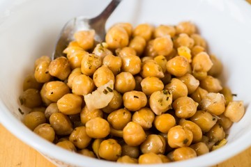 Pile of boiled chickpeas in white bowl with spoon.