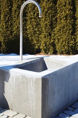 Wasserbecken mit Wasserhahn auf einem Dorfplatz, Thuja-Hecke im Hintergrund, Allgäu