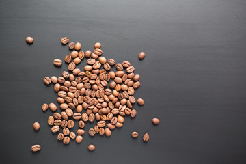 The grains of roasted coffee are scattered on a black matte surface