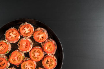 raw ground beef with fresh tomatoes lies on a frying pan standing on a black background