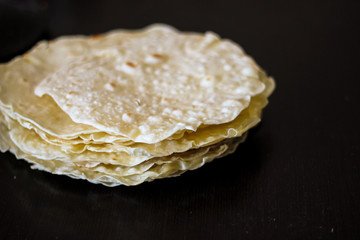 Blurred shot of homemade round tortillas stack on black table background, side view. Tortilla, lavash, flatbread or pita made of wheat flour, ingredient for cooking burrito, taco, quesadilla, sandwich