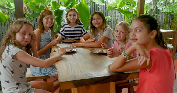 Group of multi ethnic young girls sitting at a table giving the thumbs up