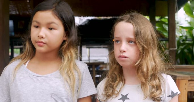 Two bored young girls standing next to each other looking off camera