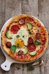 Homemade Margharita breakfast Pizza topped with fried egg sausage pepperoni on wooden background