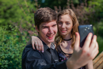 guy with a girlfriend makes a selfie in nature. young man with beautiful girl is looking at the screen of black phone.
