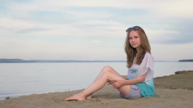 One beautiful teenage girl with brown hair outside on a beautiful summer day. The woman is sitting on the beach. The sun was gone in the sunset. She smiles, laughs, sometimes sad.