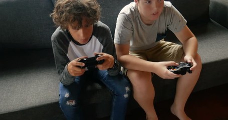 Two young 11 - 13 year old boys sitting on a sofa playing video games