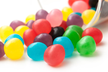 closeup of colorful round candies falling from glass container on white background .