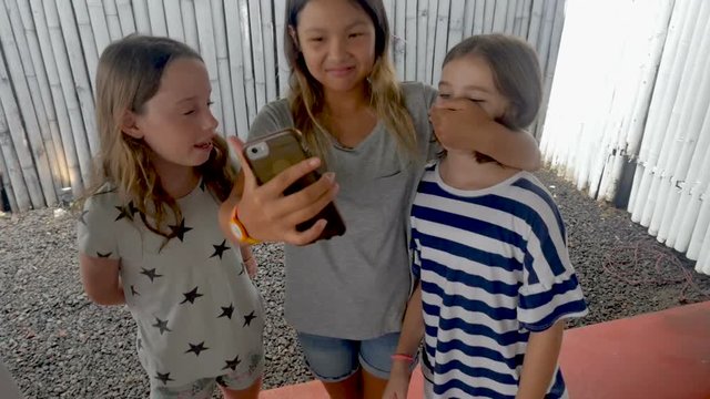 Young girl covering her friends mouth while taking a selfie with a smart phone