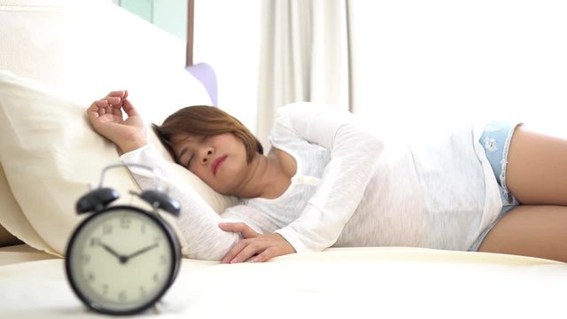 Selective focus on antique black alarm clock in front of young and beautiful asian girl on the bed.
