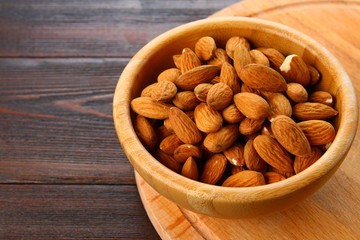 Raw dry nuts of almonds in a wooden bowl on a wooden table.