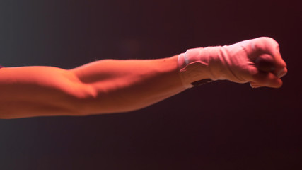 Close up shot of boxer's hands clenched into a fist on a dark red background. Fighter, boxer hand punching bag. Close-up.