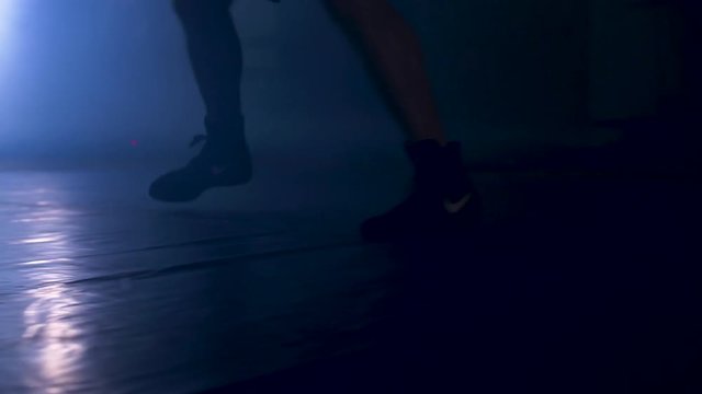 Bottom view of fighter training in the gym with smoke and light background. Silhouette of strong male boxer on dark background. Close up of athlete or sportsman moving fast while training
