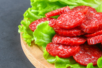 Smoked sausage, salami chopped in slices on a salad on a wooden circular cutting board on a concrete gray table.